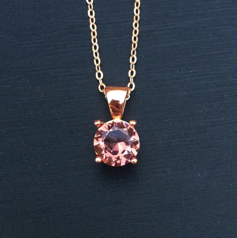 Puede incluir: Un delicado collar de cadena dorada con un colgante redondo de piedra preciosa rosa.