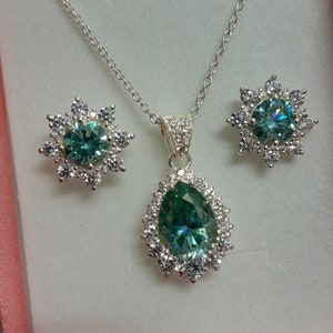 May include: A silver necklace and earrings set with a pear-shaped green gemstone surrounded by smaller clear gemstones.