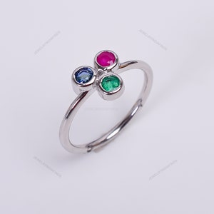 Pode incluir: Um anel de prata com três pedras preciosas: um rubi vermelho, uma esmeralda verde e um safira azul.