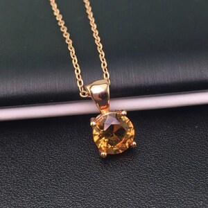 Puede incluir: Un collar de cadena de oro con un colgante redondo de piedra preciosa amarilla.