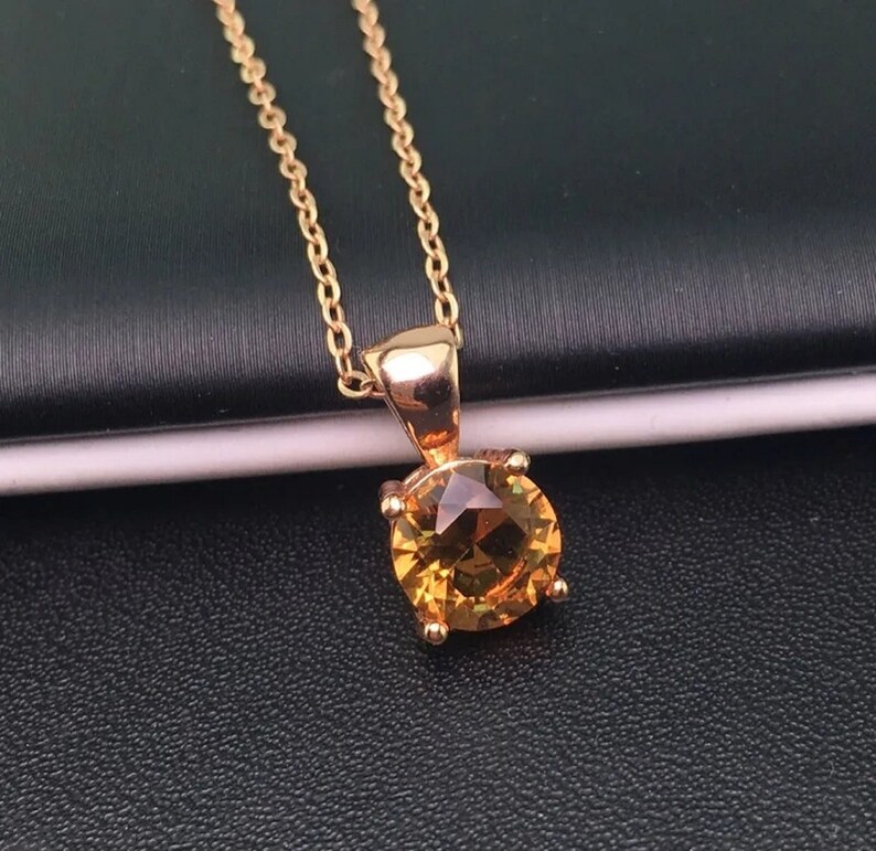 Puede incluir: Un collar de cadena de oro con un colgante redondo de piedra preciosa amarilla.