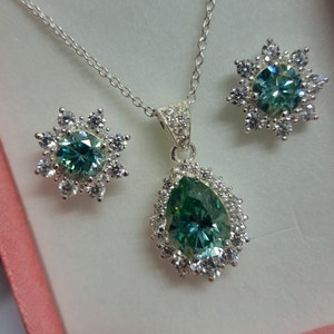 May include: A silver necklace and earrings set with a pear-shaped green gemstone surrounded by smaller clear gemstones.