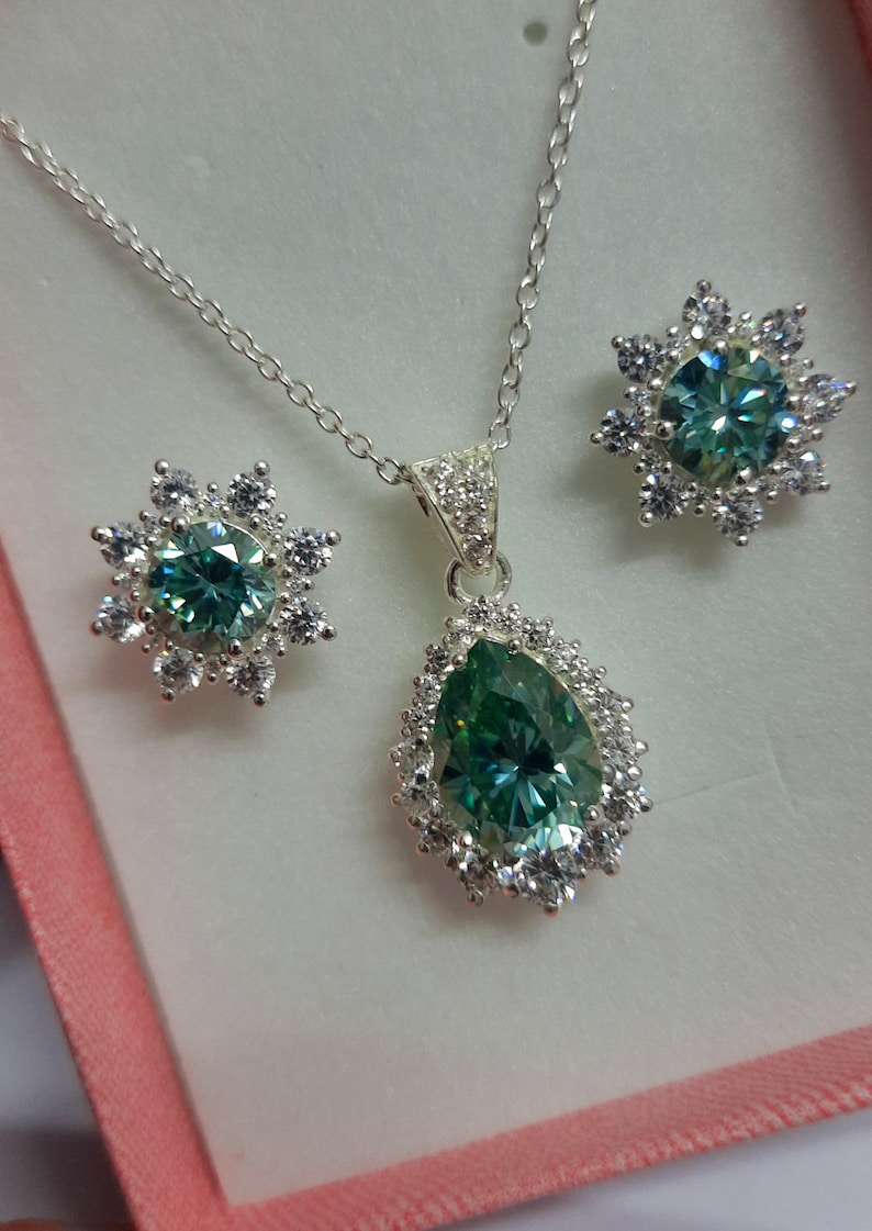 May include: A silver necklace and earrings set with a pear-shaped green gemstone surrounded by smaller clear gemstones.
