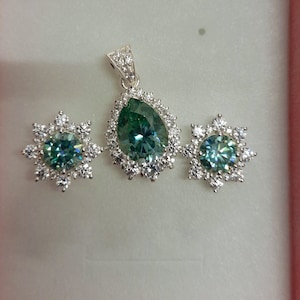 May include: A silver pendant necklace and earrings set with a pear-shaped green gemstone surrounded by smaller clear gemstones.
