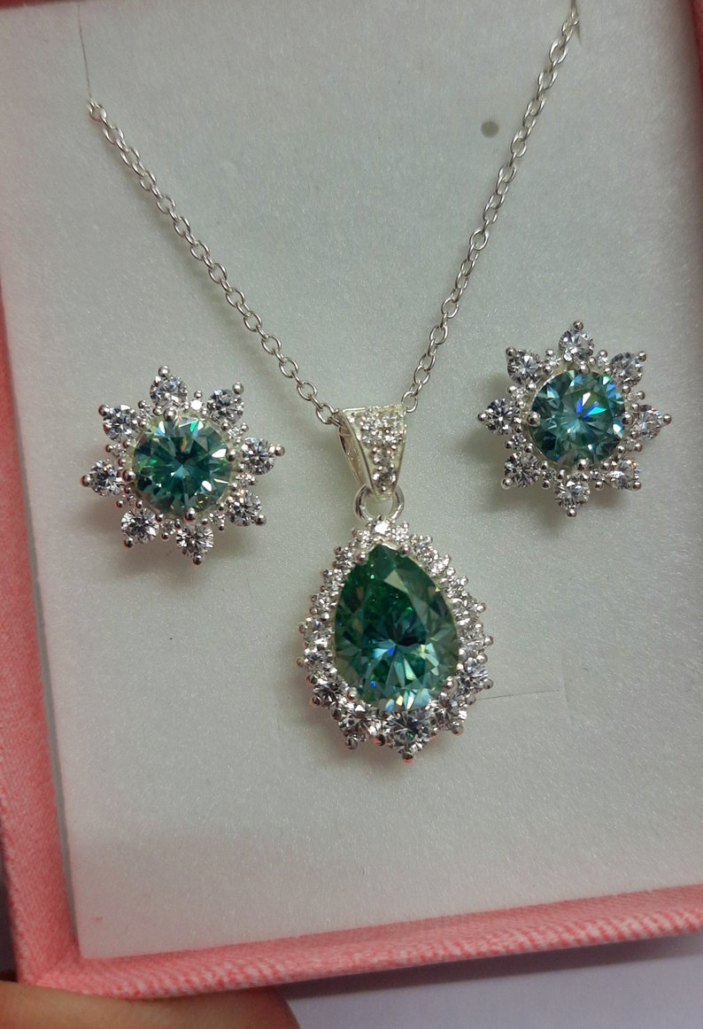May include: A silver necklace and earrings set with a pear-shaped green gemstone surrounded by smaller white gemstones.