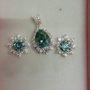 May include: A silver pendant necklace and earrings set with a pear-shaped green gemstone surrounded by smaller clear gemstones.