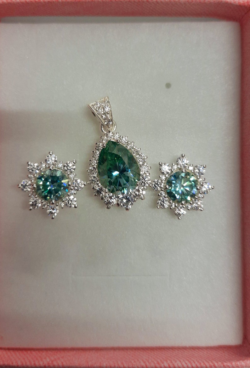May include: A silver pendant necklace and earrings set with a pear-shaped green gemstone surrounded by smaller clear gemstones.
