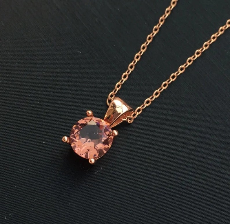 Puede incluir: Un collar de oro rosa con un colgante redondo de piedra rosa.