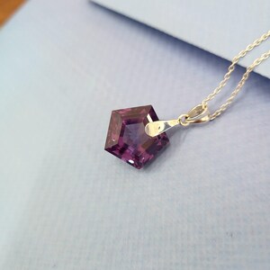 May include: A silver necklace featuring a faceted, pentagon-shaped pendant with a deep purple hue. The pendant is suspended from a delicate silver chain, creating a simple yet elegant design. The gemstone reflects light, showcasing its cut and color.