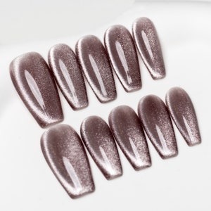 May include: Set of ten false nails with a shimmery, light brown finish. The nails are long and have a coffin shape.