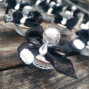 May include: A collection of small, clear glass favors with a crystal-like top and a black ribbon. Each favor has a small silver tag with the text "Thank you for celebrating with us!" printed on it.