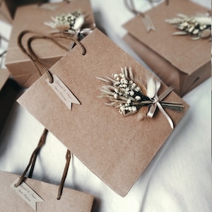 May include: Brown paper gift bags with white dried flowers and a brown ribbon. T