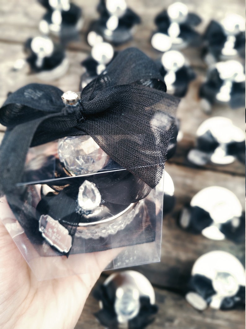 May include: A clear glass box with a black bow and a crystal-like ornament inside. The box is surrounded by other similar boxes with black bows.