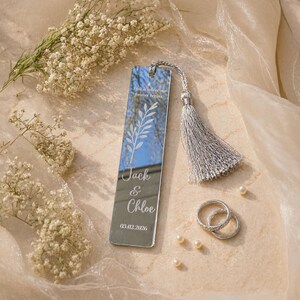 May include: A mirrored bookmark with a silver tassel, engraved with the names "Jack & Chloe" and a date. The bookmark also features the text "This is where our forever begins" and a leaf design. Two silver rings and pearls are also visible.