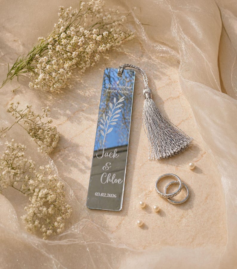 May include: A mirrored bookmark with a silver tassel, engraved with the names "Jack & Chloe" and a date. The bookmark also features the text "This is where our forever begins" and a leaf design. Two silver rings and pearls are also visible.
