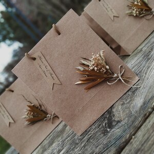 May include: Three brown paper gift bags with handles and a small bouquet of dried flowers on each.
