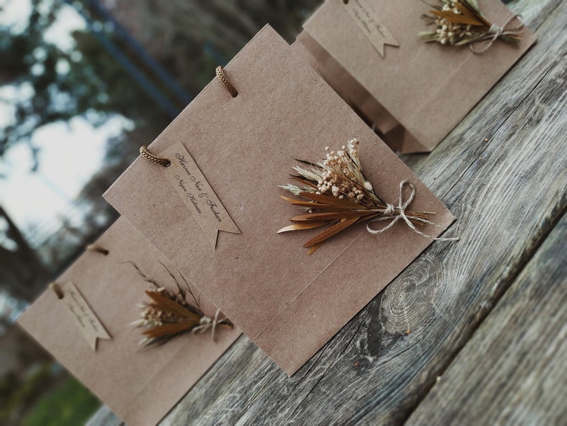 May include: Three brown paper gift bags with handles and a small bouquet of dried flowers on each.