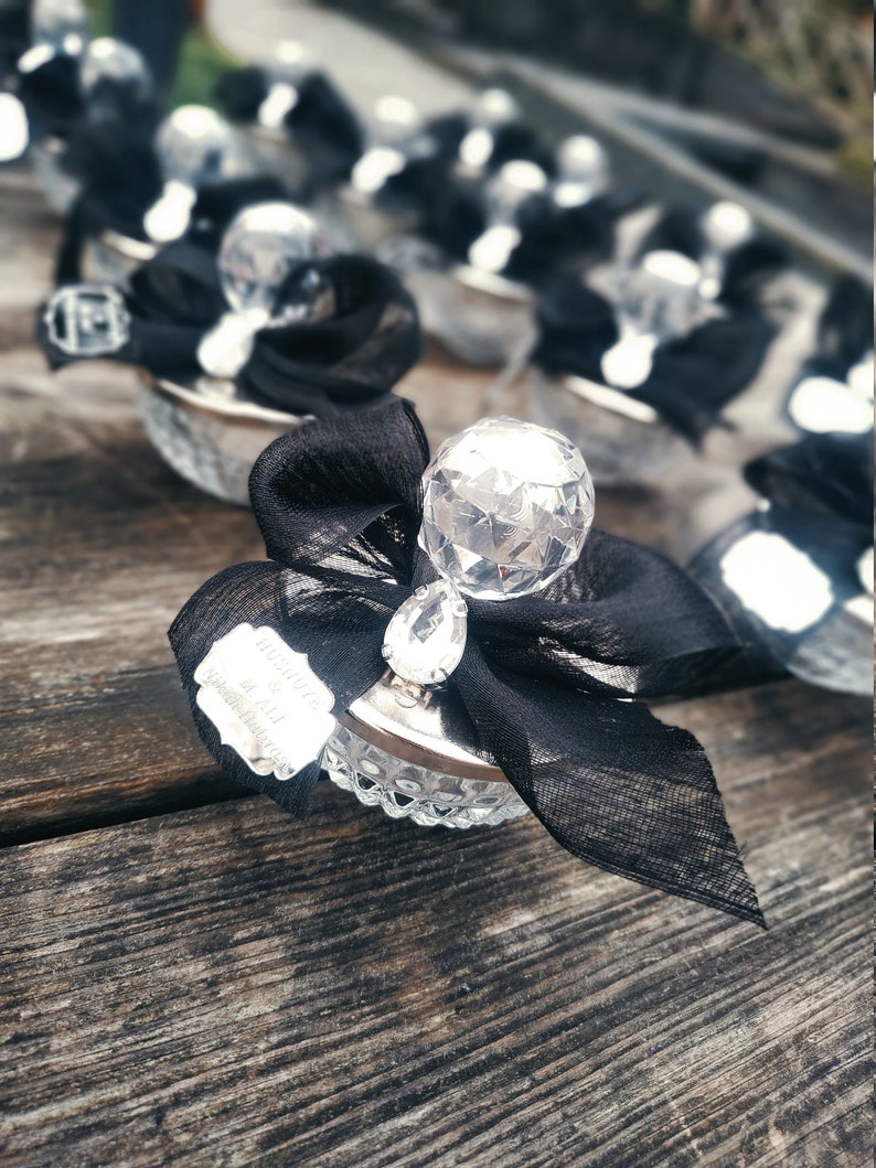 May include: A collection of small, clear glass favors with a crystal-like top and a black ribbon. Each favor has a small silver tag with the text "Thank you for celebrating with us!" printed on it.