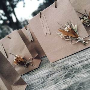 May include: A group of brown paper gift bags with dried flowers and twine accents. The bags have tags with the text