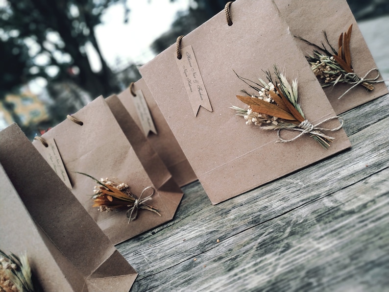 May include: A group of brown paper gift bags with dried flowers and twine accents. The bags have tags with the text