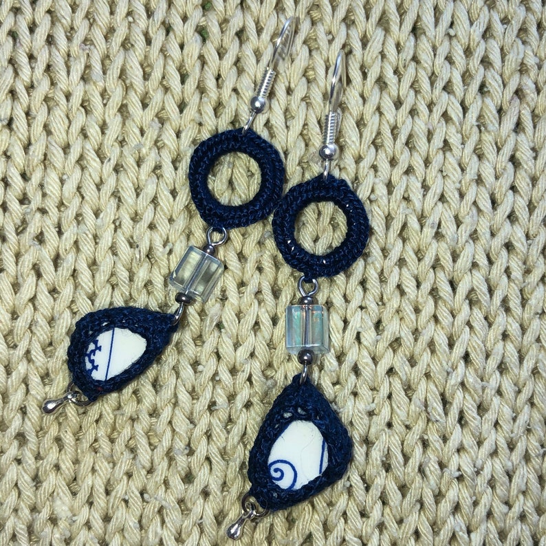 Peut inclure: Une paire de boucles d'oreilles en crochet bleu avec des accents en porcelaine blanche. Les boucles d'oreilles sont en forme de goutte et ont un motif circulaire en haut.