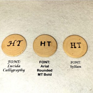 May include: Three small, round wooden discs with the initials "HT" in different fonts: Lucida Calligraphy, Arial Rounded MT Bold, and Sylfaen. The discs are light brown with visible wood grain.
