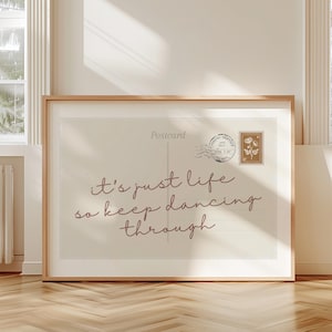 May include: A framed print with the text "It's just life so keep dancing through" in a cursive font. The print has a vintage postcard design with a stamp and postmark. The frame is a light wood color.