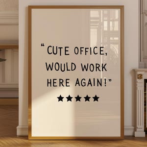 以下が含まれることがあります： 金色のフレームと黒い文字「CUTE OFFICE, WOULD WORK HERE AGAIN！」が入った額入りのプリント。テキストの下には5つの黒い星があります。プリントは木製の床のある部屋に表示されています。