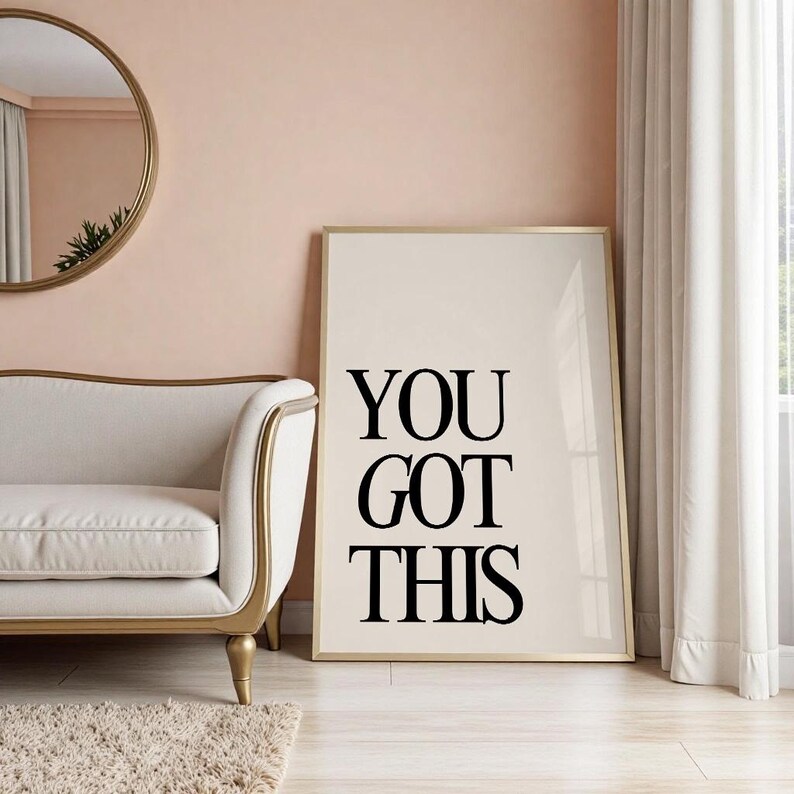 K&ouml;nnte beinhalten: Ein gerahmter Druck mit den schwarzen Worten "YOU GOT THIS" auf cremefarbenem Hintergrund. Der Druck befindet sich in einem goldenen Rahmen und lehnt an einer Wand. Der Raum hat ein Sofa, einen Spiegel und einen Teppich.