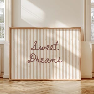 Pode incluir: Impressão emoldurada com um padrão de listras verticais em bege e branco sujo. As palavras "Sweet Dreams" são escritas em itálico em uma cor malva suave. A impressão é exibida em uma sala com luz natural.