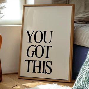 K&ouml;nnte beinhalten: Gerahmter Druck mit den Worten "YOU GOT THIS" in fetten schwarzen Buchstaben. Der Druck hat einen cremefarbenen Hintergrund und einen hellbraunen Holzrahmen. Er lehnt an einer Wand auf einem Holzboden, mit einem wei&szlig;en Teppich davor.