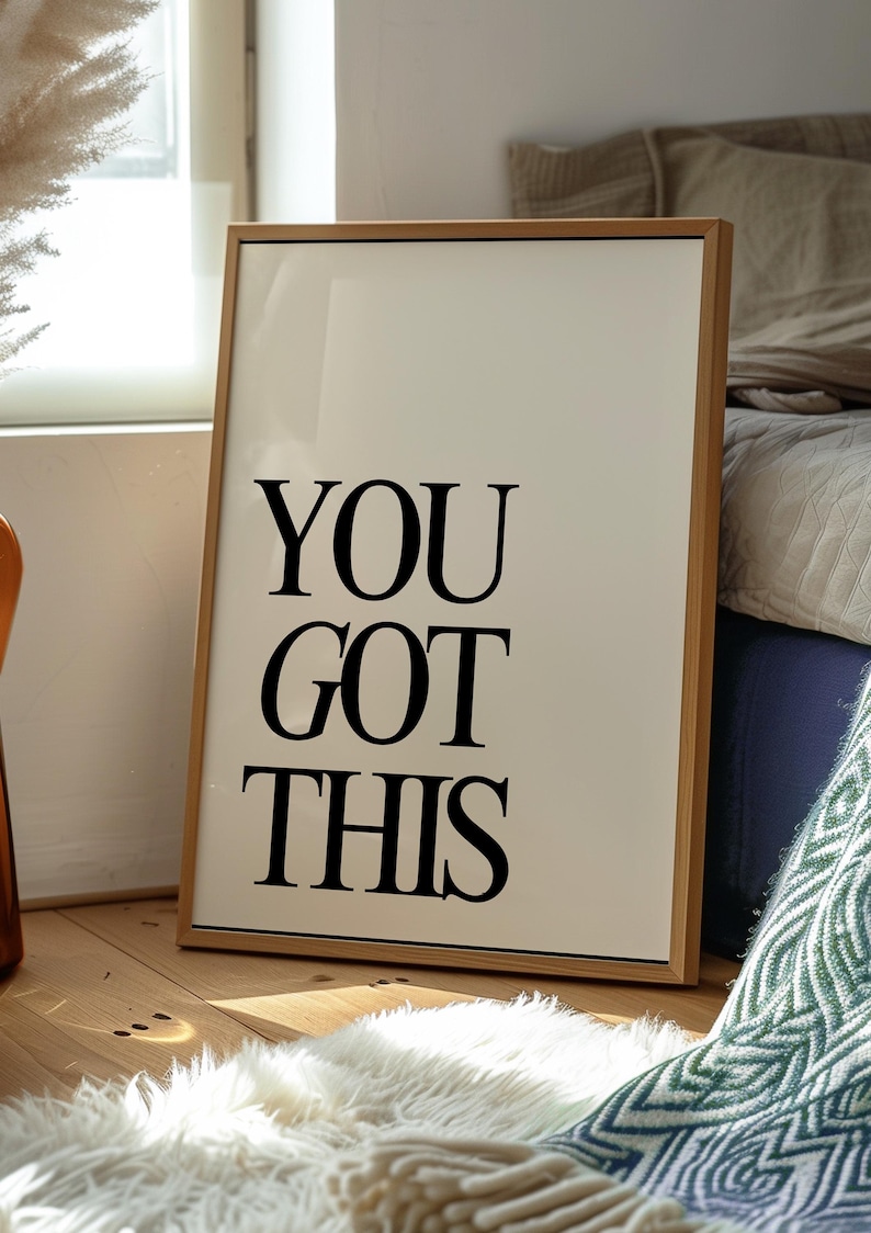 K&ouml;nnte beinhalten: Gerahmter Druck mit den Worten "YOU GOT THIS" in fetten schwarzen Buchstaben. Der Druck hat einen cremefarbenen Hintergrund und einen hellbraunen Holzrahmen. Er lehnt an einer Wand auf einem Holzboden, mit einem wei&szlig;en Teppich davor.