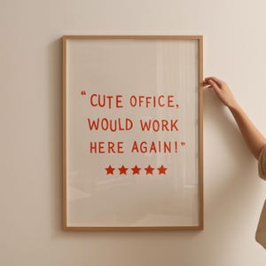 May include: Framed print with the text "CUTE OFFICE, WOULD WORK HERE AGAIN!" in red. The print has five red stars at the bottom. The frame is a light brown color.