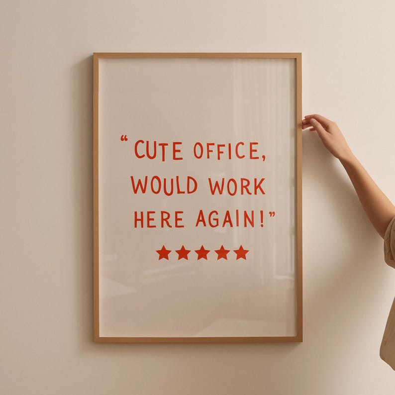 May include: Framed print with the text "CUTE OFFICE, WOULD WORK HERE AGAIN!" in red. The print has five red stars at the bottom. The frame is a light brown color.