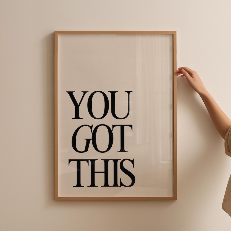 K&ouml;nnte beinhalten: Ein gerahmter Druck mit den Worten "YOU GOT THIS" in fetten schwarzen Buchstaben. Der Druck hat einen hellbeigen Hintergrund und einen d&uuml;nnen, hellbraunen Rahmen. Eine Hand ber&uuml;hrt den Rahmen.