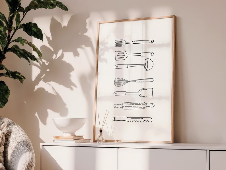 May include: A framed print featuring line drawings of kitchen utensils, including a fork, spatula, ladle, whisk, turner, rolling pin, and serrated knife. The artwork is displayed on a white cabinet with a plant and decorative items.