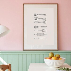 May include: A framed print featuring a series of hand-drawn kitchen utensils in black and white. The utensils include a fork, spatula, ladle, whisk, turner, rolling pin, and knife. The artwork is displayed in a room with pink and green walls.