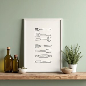 May include: A framed print featuring a black and white line drawing of various kitchen utensils. The image includes a fork, spatula, ladle, whisk, turner, rolling pin, and a serrated knife. The print is displayed on a wooden shelf.