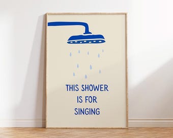 May include: A framed art print with a blue showerhead illustration and the text "THIS SHOWER IS FOR SINGING" in blue. The artwork has a cream background and a wooden frame, suitable for a bathroom.