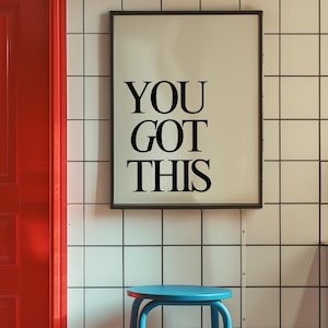 K&ouml;nnte beinhalten: Ein gerahmter Druck mit dem Text "YOU GOT THIS" in schwarzen Buchstaben. Er h&auml;ngt an einer wei&szlig; gefliesten Wand, mit einer roten T&uuml;r links und einem blauen Hocker im Vordergrund. Motivations-Thema.