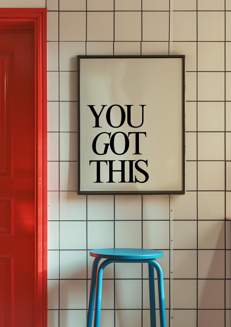 K&ouml;nnte beinhalten: Ein gerahmter Druck mit dem Text "YOU GOT THIS" in schwarzen Buchstaben. Er h&auml;ngt an einer wei&szlig; gefliesten Wand, mit einer roten T&uuml;r links und einem blauen Hocker im Vordergrund. Motivations-Thema.
