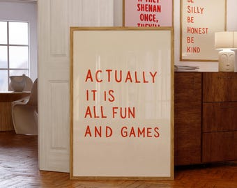 Könnte beinhalten: Ein rechteckiges gerahmtes Wandbild mit hellbeigem Hintergrund und fettgedrucktem rotem Text, der lautet: ACTUALLY IT IS ALL FUN AND GAMES. Der Rahmen besteht aus hellem Holz und der Druck steht in einem Raum mit Holzboden.