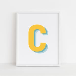 May include: A white framed print with a yellow letter C with a blue outline. The letter is in a bold, blocky font.