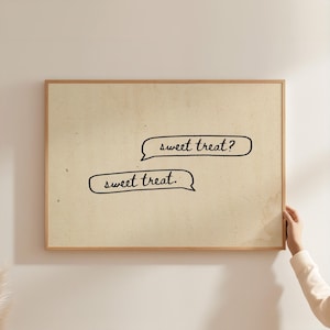 May include: A rectangular wall art print in a light wooden frame featuring a cream-colored background with two black speech bubbles. The top bubble contains the text "sweet treat?" and the bottom bubble contains the text "sweet treat."