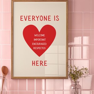 May include: A framed print with the words "EVERYONE IS HERE" in red letters. A red heart shape contains the words "WELCOME, IMPORTANT, ENCOURAGED, RESPECTED". The frame is wood-toned, set against a pink tiled wall.