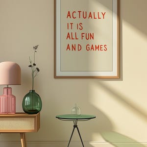 May include: A framed print with the text "ACTUALLY IT IS ALL FUN AND GAMES" in red letters. The room features a pink lamp, a green vase, and a small green table with a glass top. The floor has a black and white checkered pattern.