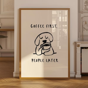 Könnte beinhalten: Ein gerahmter Kunstdruck mit beigem Hintergrund und einer schwarzen Strichzeichnung eines Hundes, der eine Kaffeetasse hält. Der Text COFFEE FIRST, PEOPLE LATER ist in schwarzer, handgezeichneter Schrift über und unter dem Hund abgebildet.
