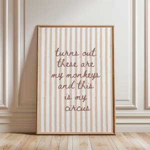 May include: Framed wall art with a beige and white striped background. The text "turns out these are my monkeys and this is my circus" is written in a brown script font. The frame is a light brown color.