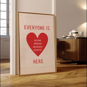 May include: A framed art print with a gold border. The print features the words "EVERYONE IS" above a red heart shape. Inside the heart are the words "WELCOME, IMPORTANT, ENCOURAGED, RESPECTED" and the word "HERE" below the heart.
