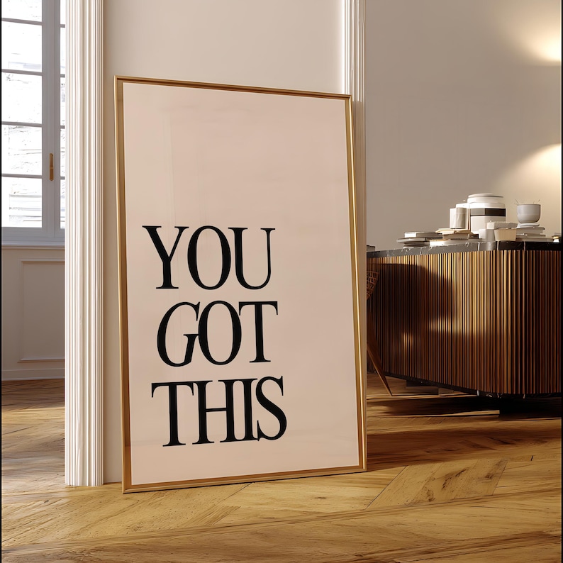 K&ouml;nnte beinhalten: Ein gerahmter Druck mit dem Text "YOU GOT THIS" in fetten schwarzen Buchstaben. Der Druck hat einen goldenen Rahmen und lehnt an einem wei&szlig;en T&uuml;rrahmen auf einem Holzboden. Im Hintergrund befindet sich ein Holzschrank.